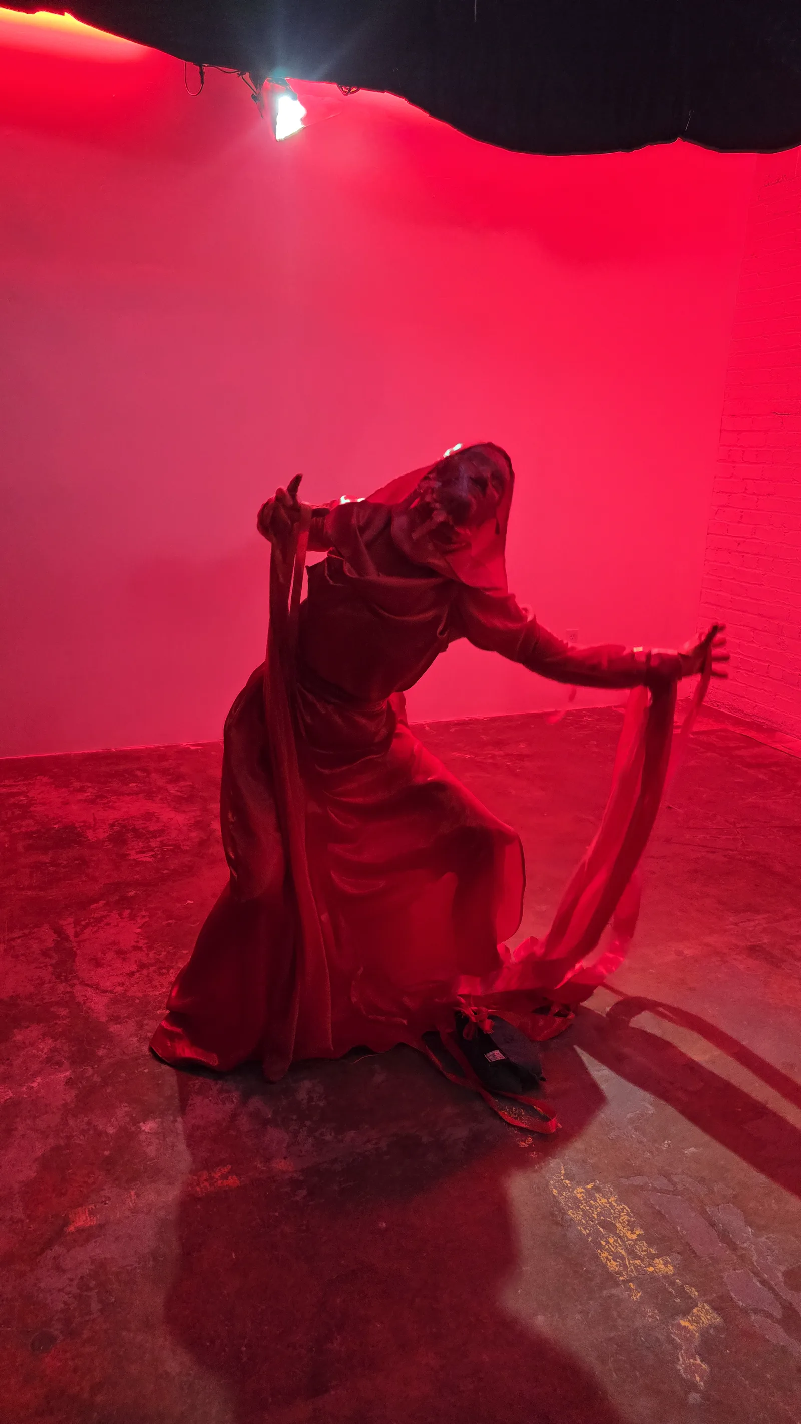The entity in full red costume, crouched on the studio floor under red light