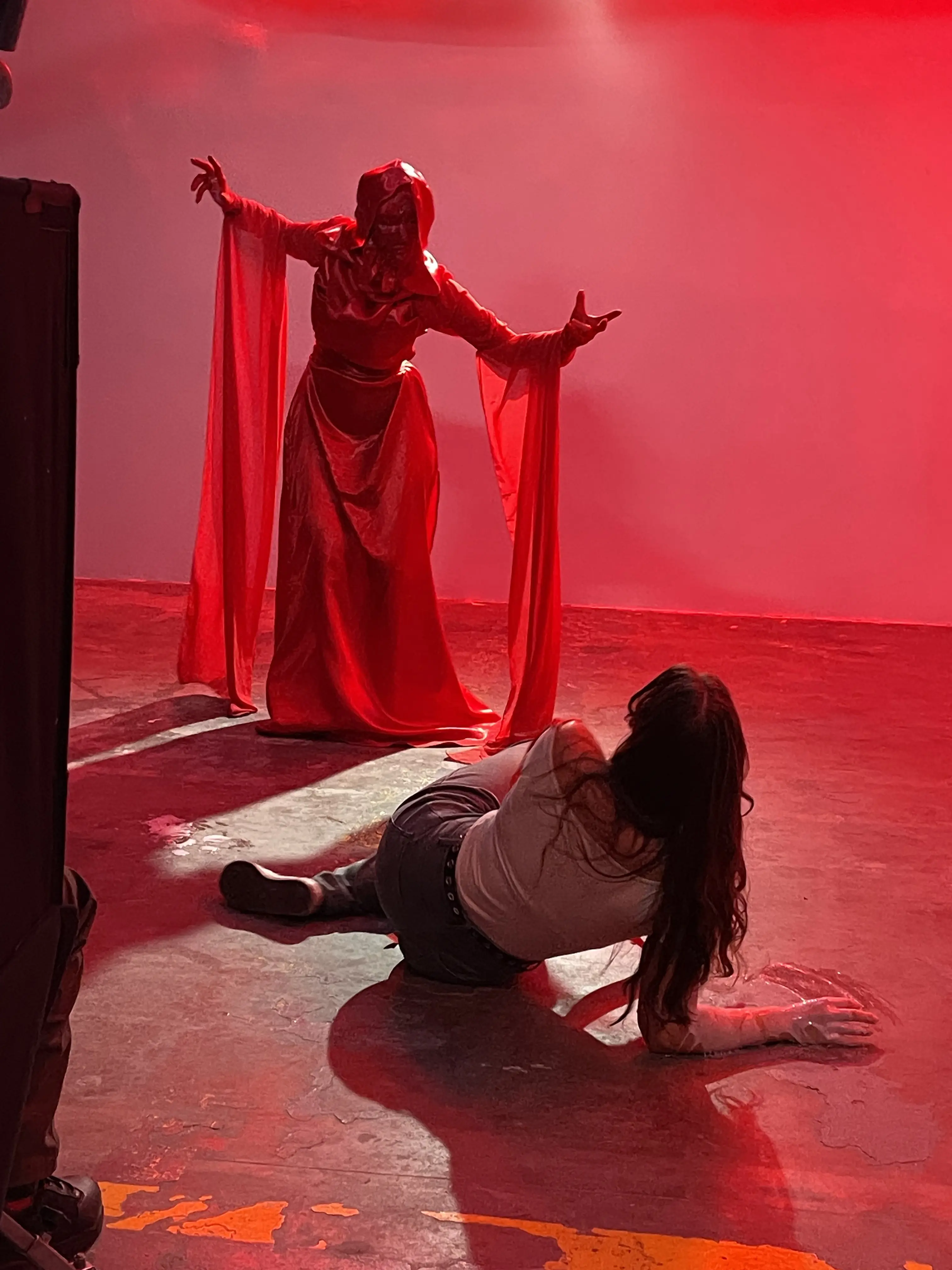 A red costumed entity confronts an actor on the floor during The Inhabitant